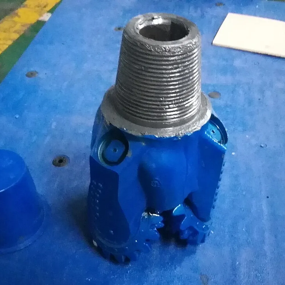 Blue tricone bit with tungsten carbide inserts standing on its pin during inspection