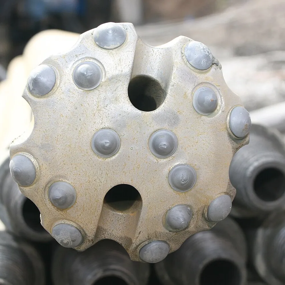 Face of a DTH button bit with carbide buttons and flushing holes, drill pipes behind
